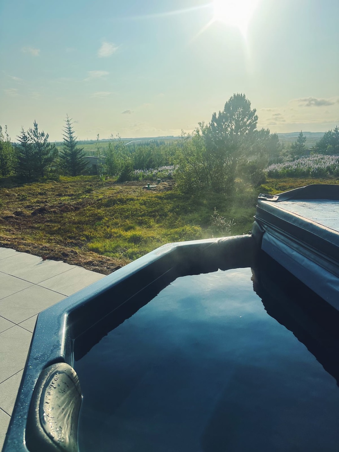 The hot tub on the tiled terrace in summer, its cover folded back and lupins on the heath beyond