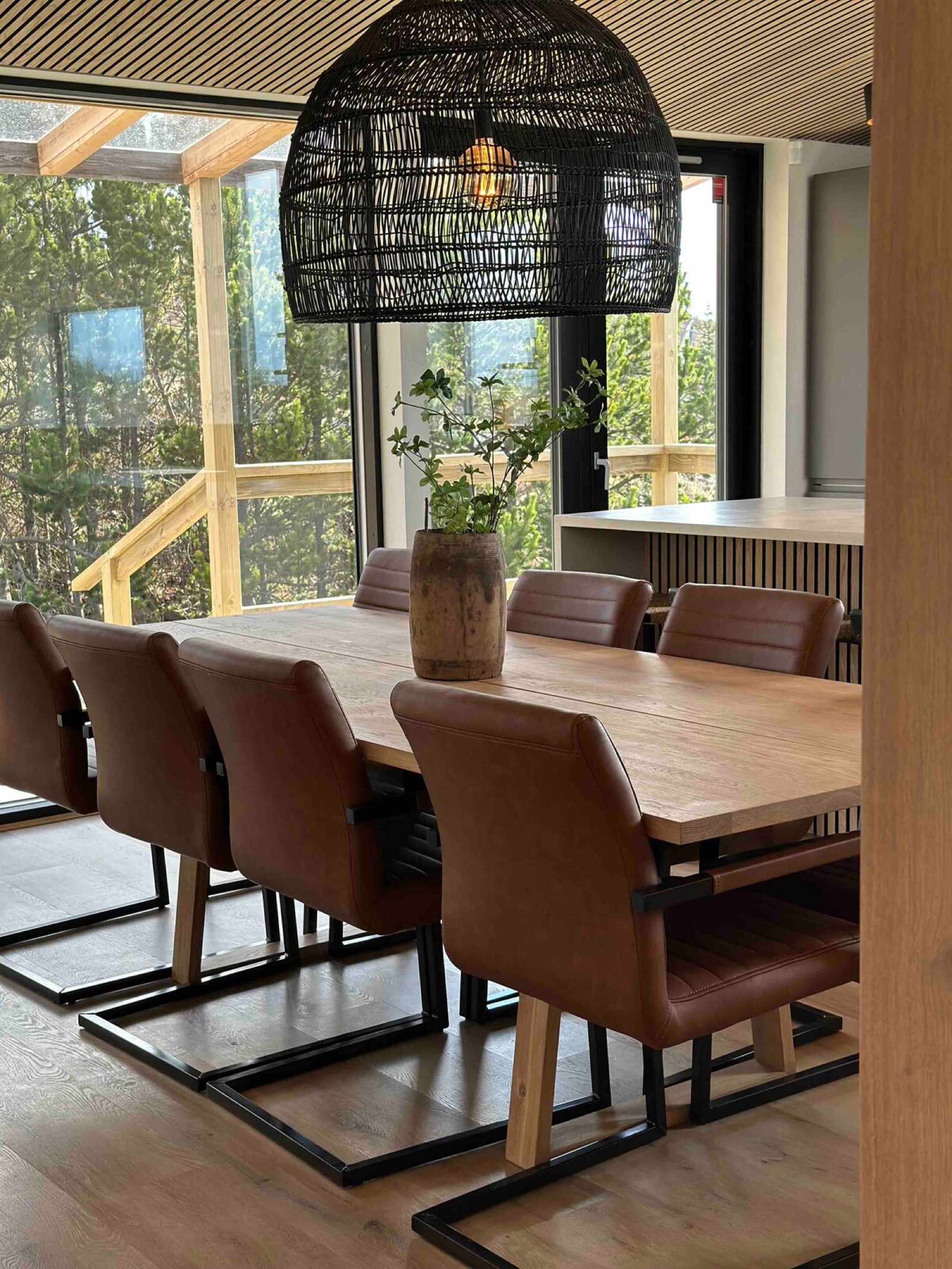 The long dining table under woven pendant shades, glazing on two sides