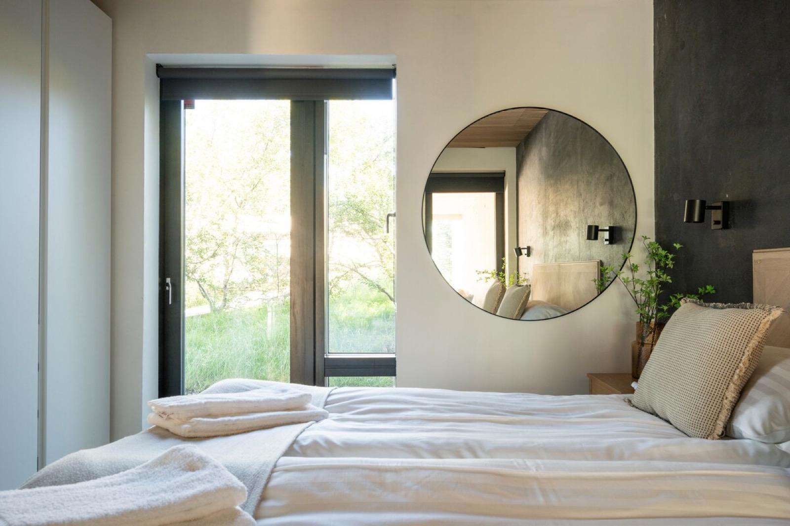 A double bedroom with a round mirror on dark plaster and a glazed door opening onto the grass