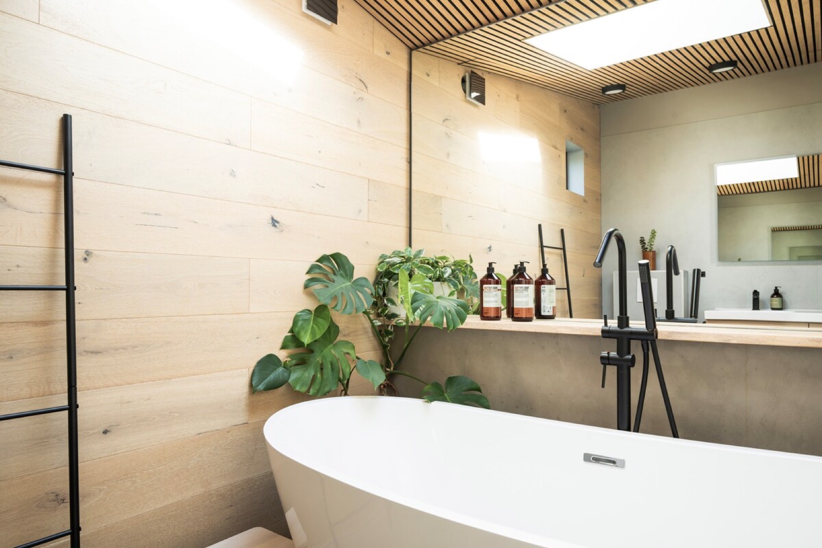 The freestanding bath below a slatted timber ceiling and a skylight