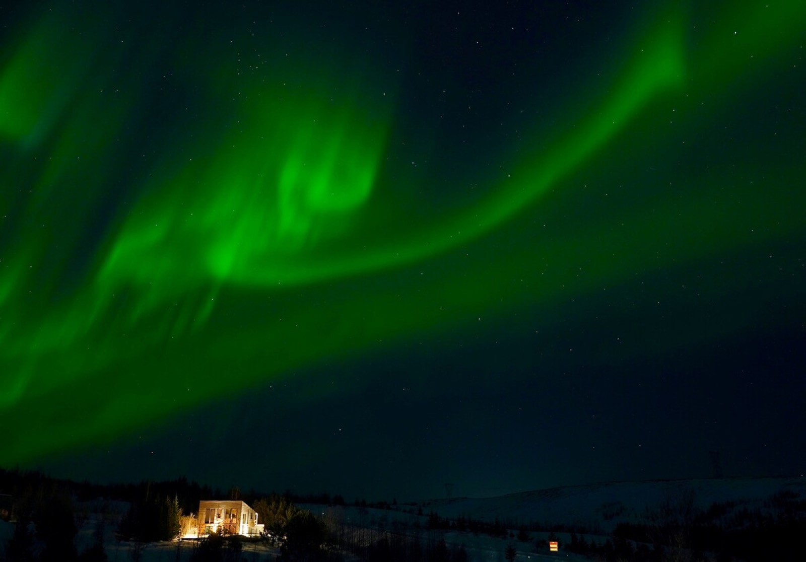 The aurora sweeping across the whole sky above the lit villa, photographed by the hosts