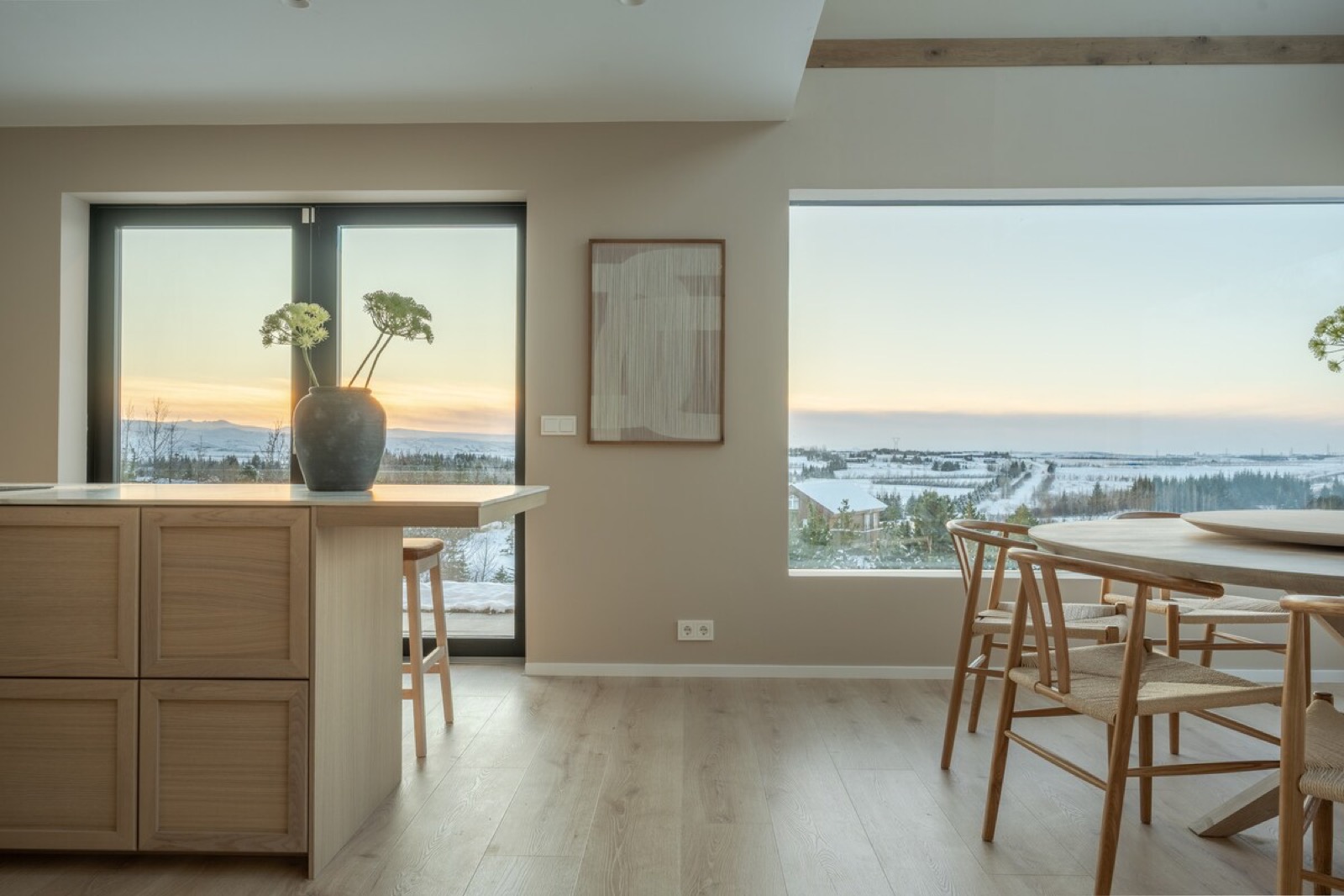The oak kitchen and its bar stools, the lowland and the sea beyond the window